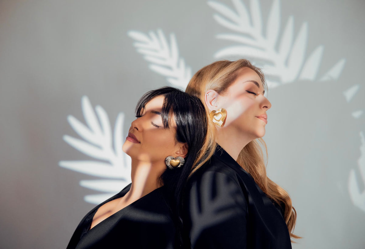 Two women wearing A l'Amour heart earrings against a sunlit wall